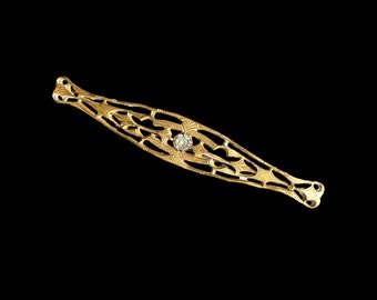 May include: A gold-toned filigree brooch with a single clear rhinestone in the center.