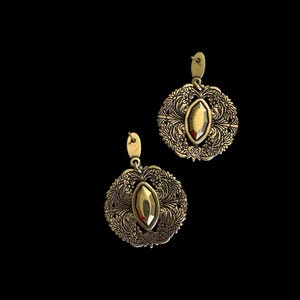 May include: A pair of gold-coloured earrings. Each earring has an oval-shaped stone at the centre, surrounded by a detailed floral design. The earrings have a hook closure and are set against a black background.
