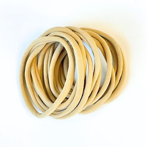 May include: A pile of 20 beige elastic hair ties. The hair ties are made of soft, stretchy fabric and are perfect for holding back hair.