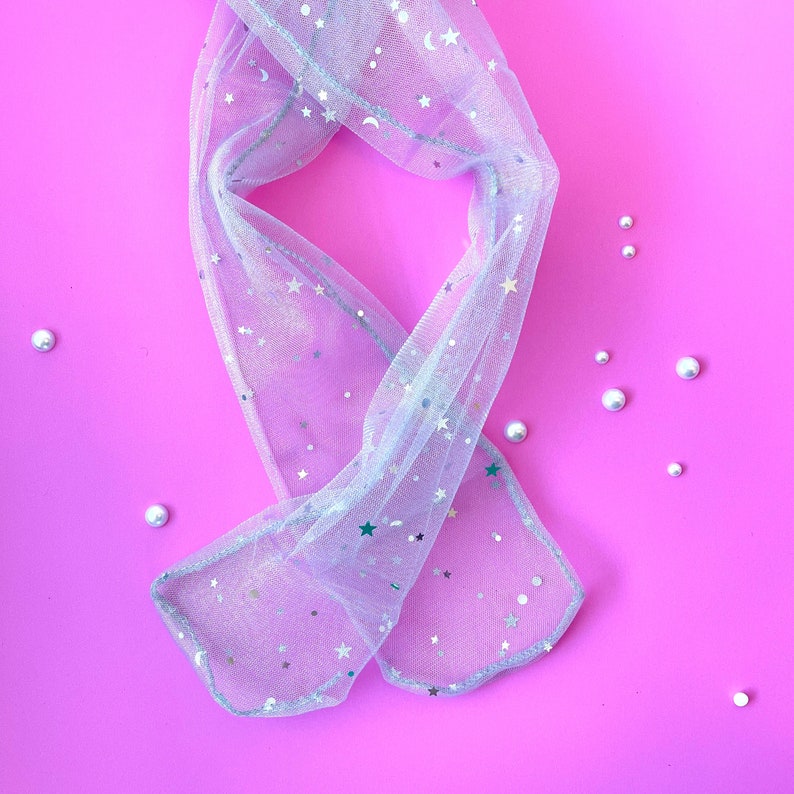 Puede incluir: Un par de medias blancas transparentes con estrellas y lunas plateadas sobre un fondo rosa.