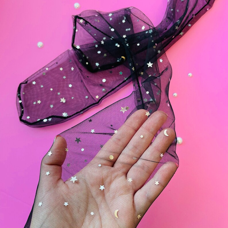 Puede incluir: Medias negras transparentes con estrellas doradas brillantes y un patr&oacute;n de media luna. Las medias est&aacute;n sobre un fondo rosa.