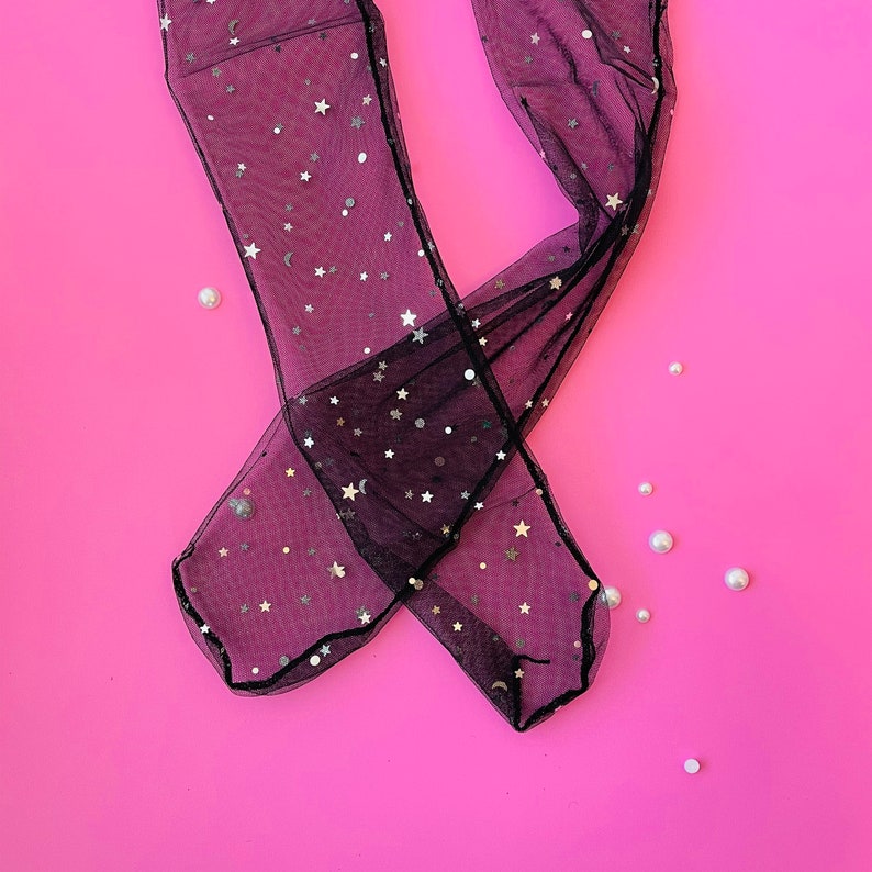 Puede incluir: Medias negras transparentes con estrellas y lunas plateadas sobre un fondo rosa.