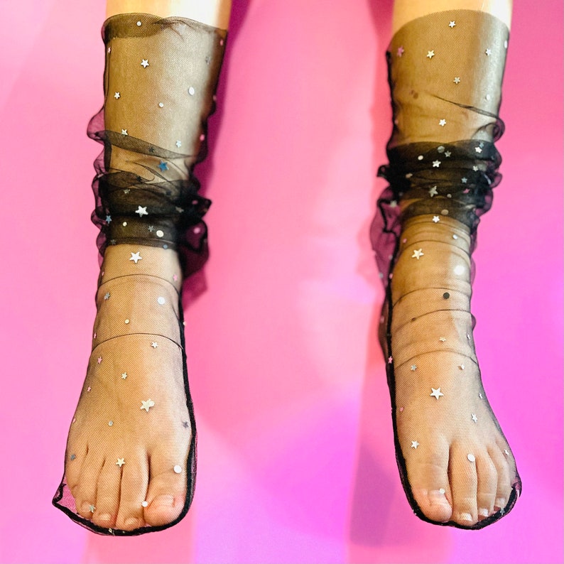 Puede incluir: Un par de calcetines negros transparentes con detalles de estrellas plateadas. Los calcetines est&aacute;n recogidos en el tobillo y se llevan en un par de pies.