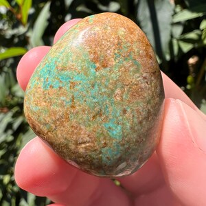 Pu&ograve; includere: Una pietra lucida e arrotondata caratterizzata da una superficie maculata con un mix di inclusioni minerali blu turchese vivace e marrone terroso. La pietra presenta una consistenza liscia e lucida e una forma organica irregolare.