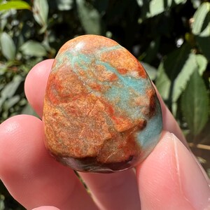 Pu&ograve; includere: Una pietra levigata e arrotondata caratterizzata da un motivo marmorizzato nei toni del blu turchese vibrante e del marrone rossastro terroso. La superficie &egrave; liscia e lucida, mostrando venature minerali naturali e variazioni di colore.