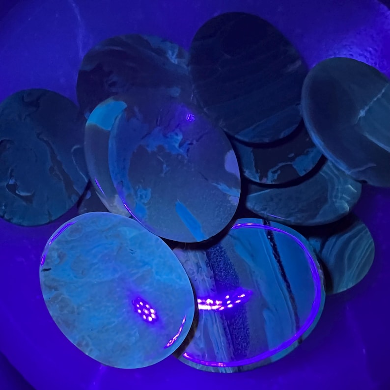 K&ouml;nnte beinhalten: Eine Ansammlung ovaler Steine mit wirbelnden Mustern in Blau- und T&uuml;rkist&ouml;nen. Die Steine werden von einem violetten Licht beleuchtet, das ihre einzigartigen Texturen und Farben hervorhebt. Eine Pr&auml;sentation von Naturstein-Kunst.