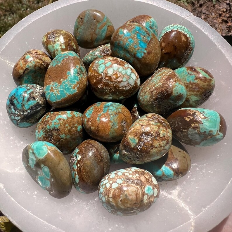 Pu&ograve; includere: Una collezione di pietre di turchese levigate e arrotondate caratterizzate da un mix di vivaci tonalit&agrave; blu-verdi e motivi a matrice marrone scuro. Le pietre sono disposte insieme in una ciotola bianca traslucida con finitura opaca.