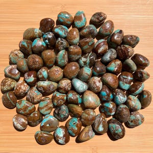 Pu&ograve; includere: Una collezione di numerose pietre levigate e arrotondate caratterizzate da un motivo marmorizzato di marrone intenso e blu turchese vibrante. Ogni pietra ha una superficie liscia e lucida con venature uniche, creando un mix di colori terrosi.