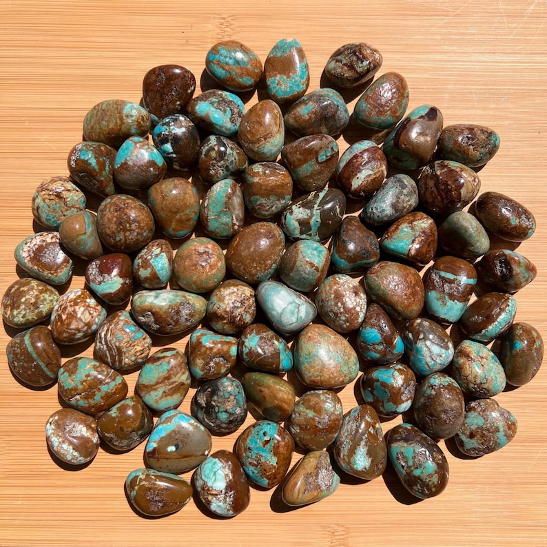 Pu&ograve; includere: Una collezione di numerose pietre levigate e arrotondate caratterizzate da un motivo marmorizzato di marrone intenso e blu turchese vibrante. Ogni pietra ha una superficie liscia e lucida con venature uniche, creando un mix di colori terrosi.