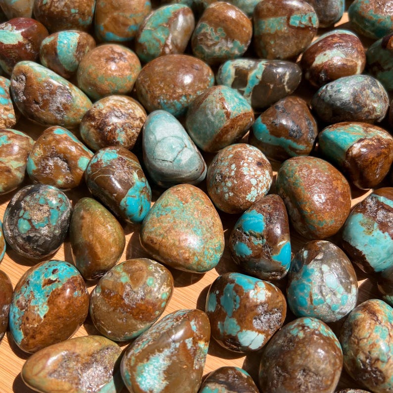 Pu&ograve; includere: Una collezione di pietre levigate e burattate che presentano un mix di colori marrone e blu turchese. Ogni pietra ha una superficie liscia e arrotondata con venature naturali e motivi irregolari, mostrando una miscela di toni terrosi e blu.