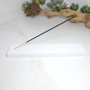 May include: White rectangular incense holder with a black incense stick resting on top.