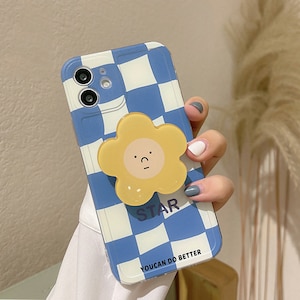 May include: A blue and white checkered phone case with a yellow flower-shaped phone grip. The grip has a cartoon face with a sad expression. The text "STAR" and "YOU CAN DO BETTER" is printed on the case.
