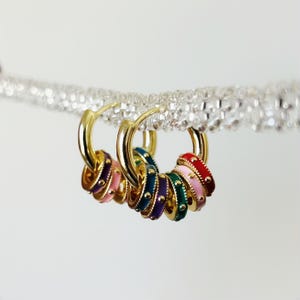 May include: Gold hoop earrings with colorful enamel rings. The rings are stacked and feature a variety of colors, including pink, red, green, and purple.