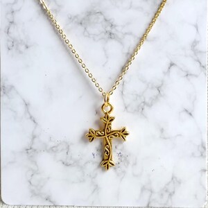 Peut inclure: Un collier en chaîne dorée avec un pendentif en forme de croix orné. La croix est ornée de motifs floraux complexes.