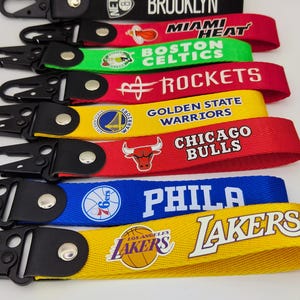 May include: A set of colorful keychains featuring NBA team logos, including the Miami Heat, Boston Celtics, Houston Rockets, Golden State Warriors, Chicago Bulls, Philadelphia 76ers, and Los Angeles Lakers.