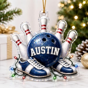 May include: A decorative acrylic ornament featuring a blue bowling ball with the name AUSTIN printed in white, surrounded by four white bowling pins with red stripes, a pair of blue and white bowling shoes, and a string of colorful Christmas lights.