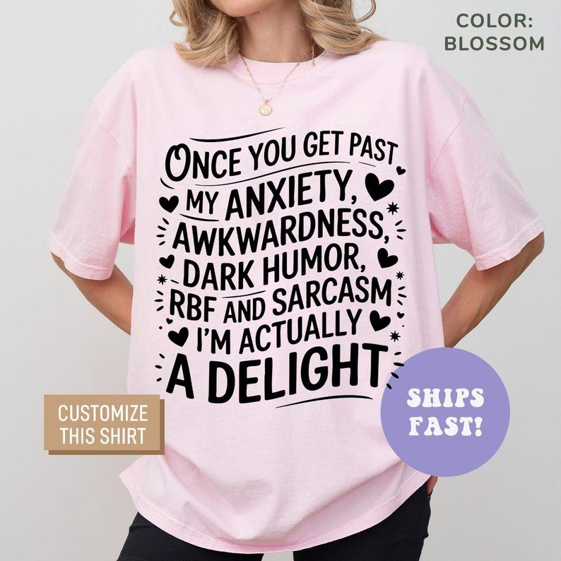 May include: Pink t-shirt with black text that reads "Once you get past my anxiety, awkwardness, dark humor, RBF and sarcasm I'm actually a delight".