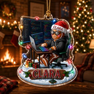 May include: A decorative acrylic ornament featuring a gingerbread person wearing a Santa hat with the name CLARA, sitting at a desk with a laptop and computer monitors displaying code. The base has a wooden sign reading CLARA with small gifts.