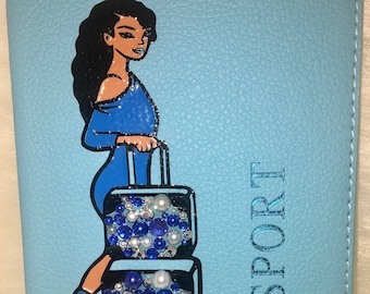May include: A light blue passport holder featuring a woman in a blue dress holding a suitcase decorated with blue and white embellishments. The word "PASSPORT" is printed on the front of the holder.