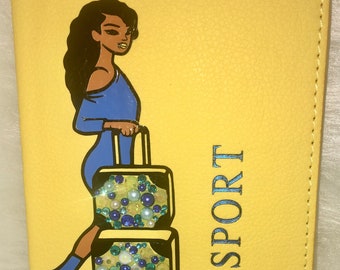 May include: Yellow passport holder featuring a woman in a blue dress and a suitcase adorned with rhinestones. The suitcase has wheels and a handle. The text "PASSPORT" is printed on the holder in blue.