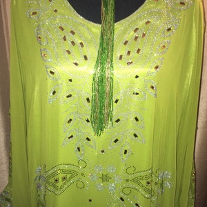 May include: A lime green kaftan with a beaded neckline and a beaded tassel. The kaftan is covered in rhinestones and has a paisley design.