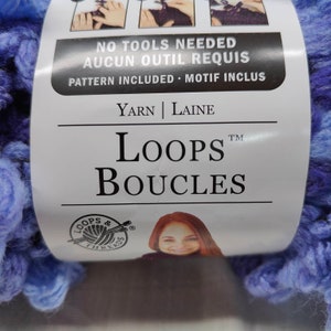 May include: A skein of Loops & Threads Loops Boucles yarn in a blue and purple colorway. The label reads "No tools needed.  Aucun outil requis.  Pattern included.  Motif inclus.  Yarn | Laine.  Loops™ Boucles."