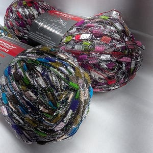 May include: Close-up of three colorful yarn skeins. The yarn is a mix of colors including purple, pink, green, blue, and silver. The yarn is labeled "City Life" and "Premier Yarns". The yarn is on a white surface.
