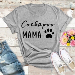 May include: Gray t-shirt with the text "Cockapoo Mama" and a black paw print.