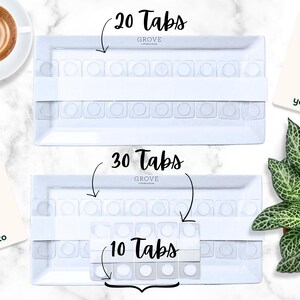K&ouml;nnte beinhalten: Zwei wei&szlig;e Tabletts mit Tab-Eins&auml;tzen, beschriftet mit "20 Tabs", "30 Tabs" und "10 Tabs". Die Tabletts sind rechteckig mit abgerundeten Ecken. Das Bild enth&auml;lt auch eine Tasse Kaffee, eine Pflanze und Karten mit "Make Your Own" und "yoto".