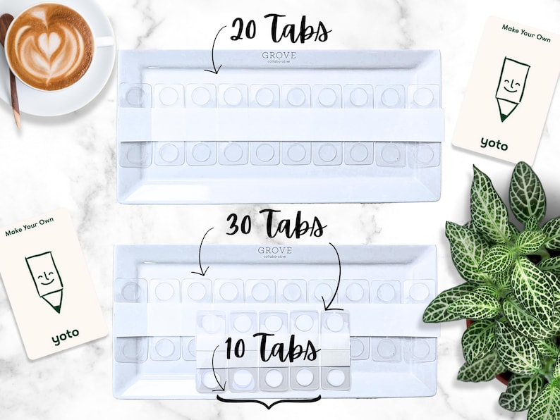 K&ouml;nnte beinhalten: Zwei wei&szlig;e Tabletts mit Tab-Eins&auml;tzen, beschriftet mit "20 Tabs", "30 Tabs" und "10 Tabs". Die Tabletts sind rechteckig mit abgerundeten Ecken. Das Bild enth&auml;lt auch eine Tasse Kaffee, eine Pflanze und Karten mit "Make Your Own" und "yoto".