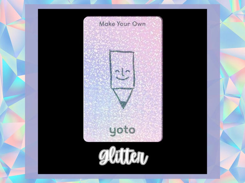 Op de afbeelding: Een witte kaart met een glinsterende textuur en een tekening van een lachend potlood. De kaart heeft bovenaan de tekst "Make Your Own" en onderaan "yoto". De tekst "glitter" staat onder de kaart.