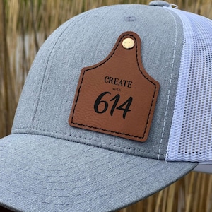 May include: A gray and white trucker hat with a brown leather patch that says "CREATE with 614".