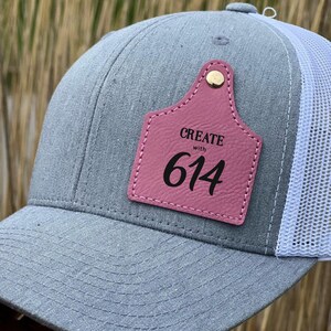 May include: A gray and white trucker hat with a pink leather patch that says "CREATE with 614".