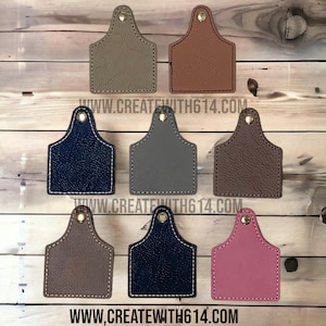 May include: Nine leather tags in various colors, including brown, tan, gray, black, and pink. Each tag has a gold metal ring at the top and a stitched border. The tags are arranged in three rows on a wooden surface. The text "www.createwith614.com" is visible at the bottom of the image.