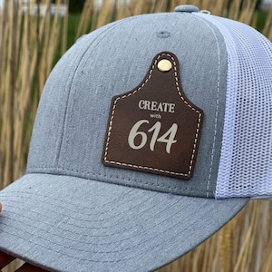 May include: A gray and white trucker hat with a brown leather patch that says "CREATE with 614".