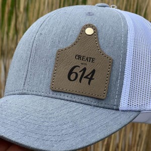 May include: A gray and white trucker hat with a brown leather patch that says "CREATE with 614".