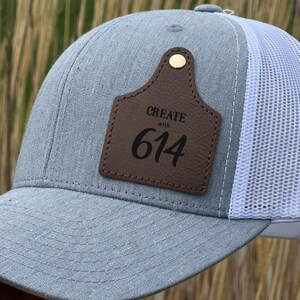 May include: A gray and white trucker hat with a brown leather patch that says "CREATE with 614".