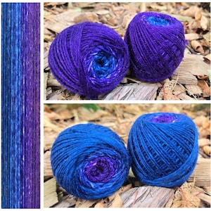 May include: Four round balls of yarn featuring a variegated color palette of deep purple, royal blue, and lighter azure tones. The yarn displays a consistent twisted texture with a smooth finish, showcasing a gradient of blended cool colors.