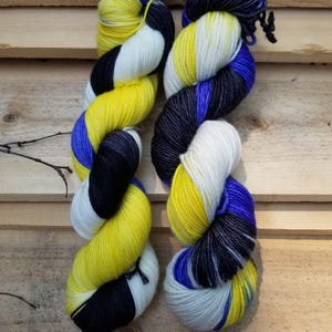 May include: Two skeins of colorful yarn in a wooden setting. The yarn is a mix of yellow, blue, black, and white. The yarn is twisted and appears soft. The yarn is likely for knitting or crocheting projects.