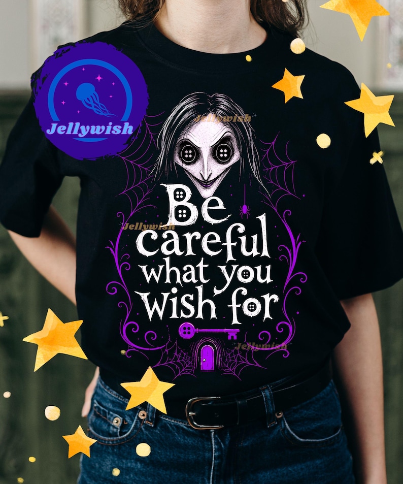 May include: Black t-shirt featuring a graphic of a character with button eyes and the text "Be careful what you wish for" in white and purple. The design includes a key and spiderwebs.