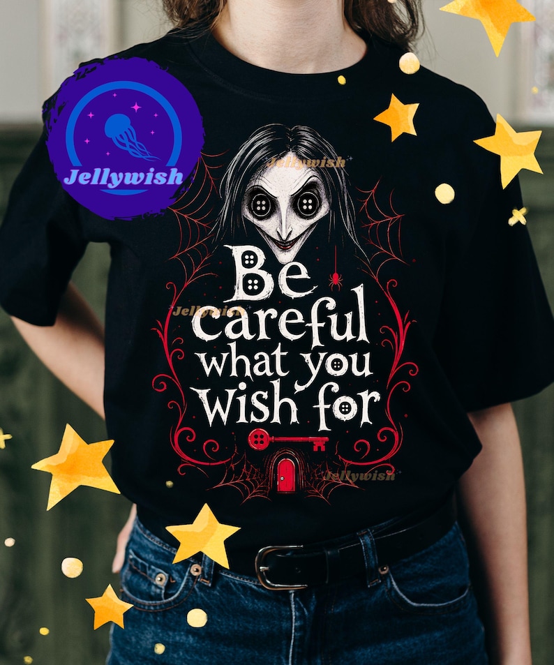 May include: Black t-shirt featuring a stylized illustration of a character with button eyes and the text "Be careful what you wish for." The design includes a spiderweb, key, and door in red and white.