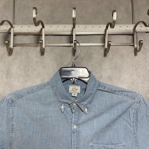 Op de afbeelding: Een lichtblauw overhemd met knopen, een kraag en een borstzak, hangend aan een zwarte hanger. Het shirt is gemaakt van een textuurstof en heeft een klein merklabel op de borst. Het shirt is maat M.