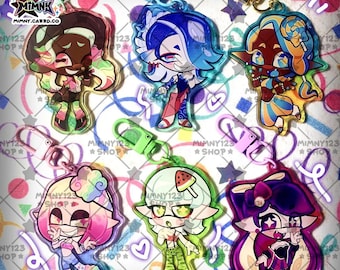 May include: A collection of colorful acrylic keychains featuring anime-style characters. Each keychain has a unique design with vibrant colors, including pink, blue, green, and purple. The keychains are attached to metal clasps.