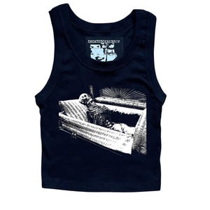 May include: A black tank top with a white graphic of a skeleton in a coffin. The tank top has the text "DECAYEDCEREBRUM" on a small tag near the neckline. The graphic is detailed and appears to be a pen and ink drawing.