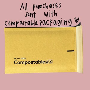 May include: A brown paper envelope with the text "Hi, I'm 100% Compostable" and a compostable logo. The envelope has a black line across the top and the text "All purchases sent with Compostable Packaging &hearts;" is written above the envelope.
