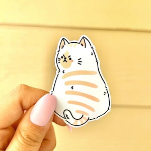 May include: A white and orange cartoon cat sticker with a grumpy expression. The cat is facing away from the viewer and has a striped tail.