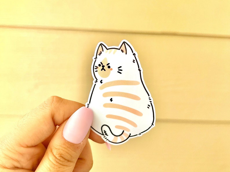 May include: A white and orange cartoon cat sticker with a grumpy expression. The cat is facing away from the viewer and has a striped tail.