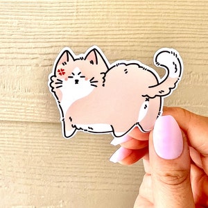 May include: A pink and white cartoon cat sticker with a red flower on its eye. The cat is sitting on its hind legs with its tail curled around its body.