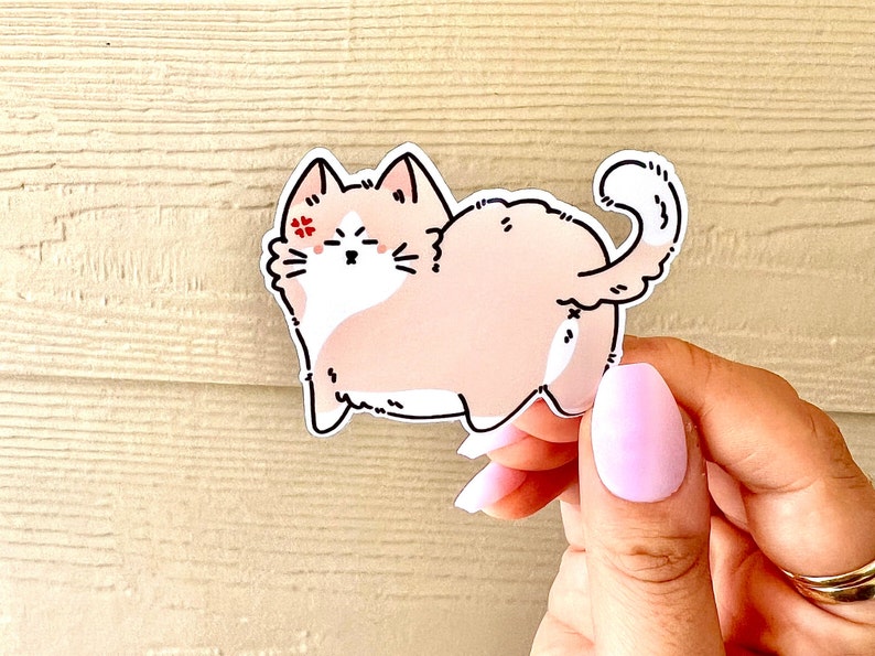 May include: A pink and white cartoon cat sticker with a red flower on its eye. The cat is sitting on its hind legs with its tail curled around its body.