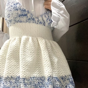 May include: A white crochet dress with a blue and white crocheted bodice. The dress has a fitted bodice and a full skirt.